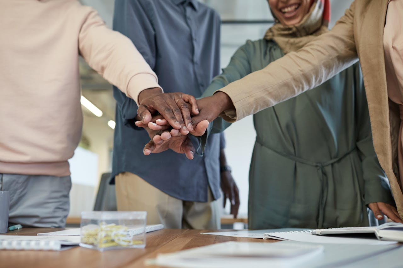 home-img A diverse group of colleagues stacking hands, representing teamwork and unity in an office environment.